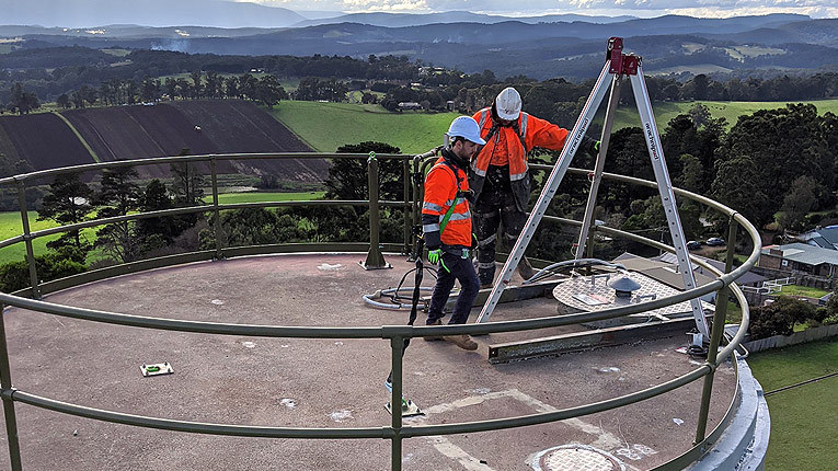 Two individuals in high-vis attire repairing water tank in Gembrook