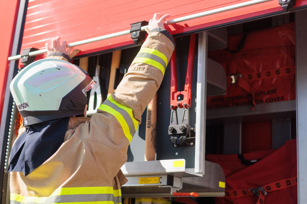 A firefighter is loading tools into a fire truck, preparing for an emergency response.